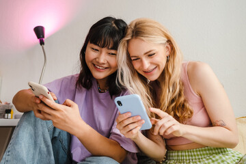 Two multiracial girls laughing while using mobile phones together