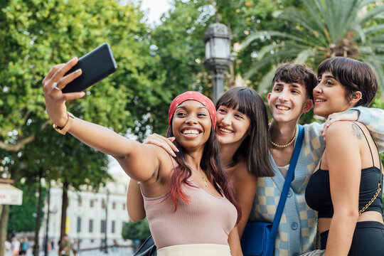 Happy Woman With Friends Taking Selfie Through Mobile Phone In Park