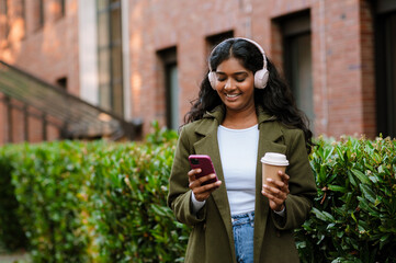 Brunette woman using mobile phone and drinking coffee at city street