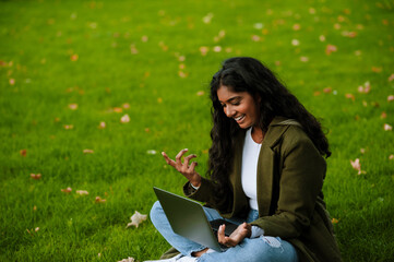 Brunette indian woman smiling and working with laptop in park