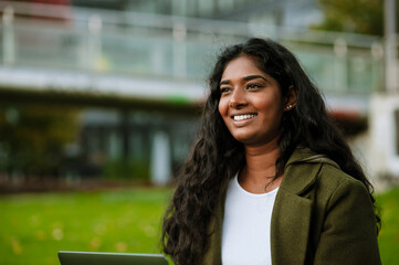 Brunette indian woman smiling and working with laptop in park