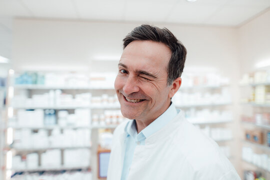 Happy pharmacist in lab coat winking at store