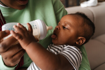 Young black woman feeds baby with bottle infant formula
