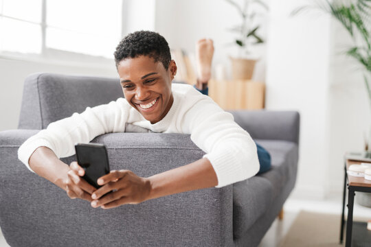 Smiling Woman Lying On Couch Using Mobile Phone