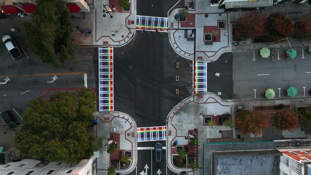 LGBTQ queer theme. Rainbow pride crosswalk pedestrian walkway on street in American urban college town. Rising aerial.