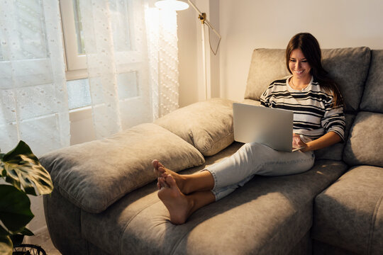 Happy Woman Using Laptop On Sofa At Home