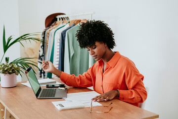 Freelancer sitting with laptop and examining financial bills at desk