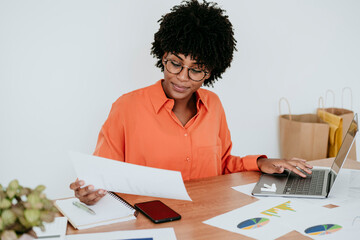 Businesswoman with laptop examining documents at desk in home office