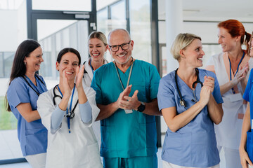Portrait of happy doctors, nurses and other medical staff clapping in hospital.
