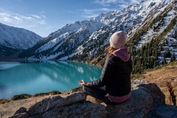 Naklejka na ściany i meble Woman meditating on a vantage point over turquoise lake surrounded by mountains