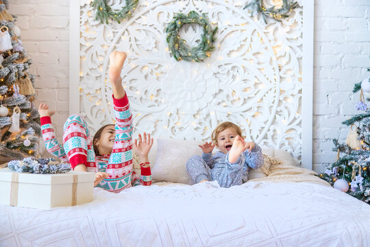 Children jump on the bed near the Christmas tree. Selective focus.