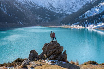 Romantic couple standing on a boulder on a vantage point over mountain lake