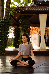 White brunette woman doing yoga while sitting on wooden floor outdoors