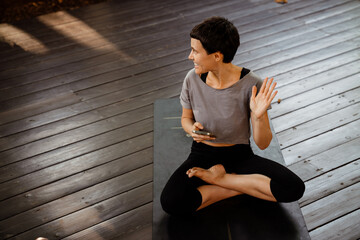 White woman using cellphone while doing yoga on wooden floor outdoors