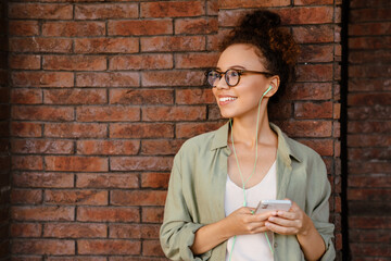 White young woman smiling while using earphones and cellphone outdoors