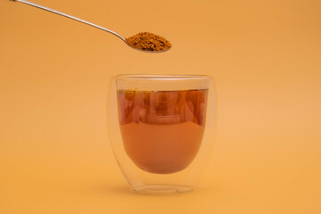 Female hand pouring instant coffee into double layer clear glass with boiled water with spoon on vintage color background.