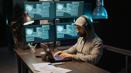 Hacker coder hacking system at night using virus to produce computer malware and server error. Data thief stealing information from software app, working with multiple monitors. Handheld shot. © DC Studio