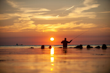 Fototapeta premium Rear view of man fishing in sea at sunset