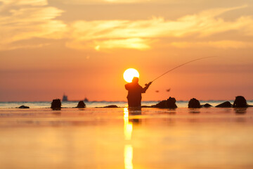 Fototapeta premium Rear view of man fishing in sea at sunset