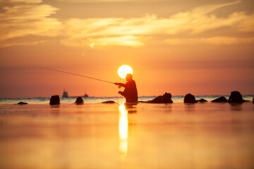 Rear view of man fishing in sea at sunset