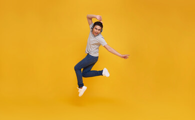Fototapeta na wymiar Young handsome Asian man smiling and jumping wearing wireless headphone listening to music isolated over yellow background.