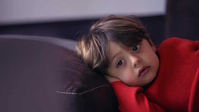 Closeup little boy face lying on sofa watching cartoon. Child hypnotized by media entertainment. Small boy resting at home