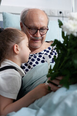 Little girl giving flowers bouquet present, hugging grandfather admitted to hospital. Elderly...