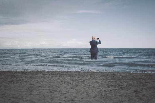 Businessman standing in the sea and taking pictures