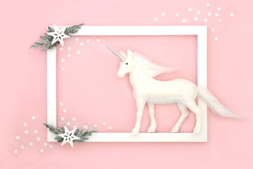 Christmas magic background with unicorn and snowflake decorations with snow covered fir and white frame on pastel pink,. Festive fun border magical design for Xmas and New Year. © marilyn barbone