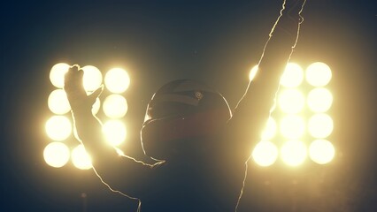 Silhouette of race car driver celebrating the win in a race against bright stadium lights. 100 FPS...