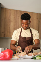 Fototapeta na wymiar Young african man preparing a chicken mince recipe in a kitchen.