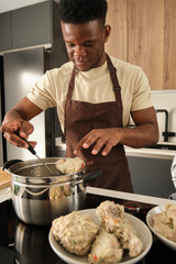 Fototapeta na wymiar Young african man preparing boiled chicken mince with vegetables recipe in a kitchen.