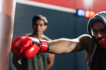 Caucasian man wear boxing gloves punching ahead with trainer in gym. 