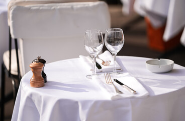 Restaurant terrace table prepared for guests and clients. A white table with forks knife and wine glass on the terrace of a restaurant.