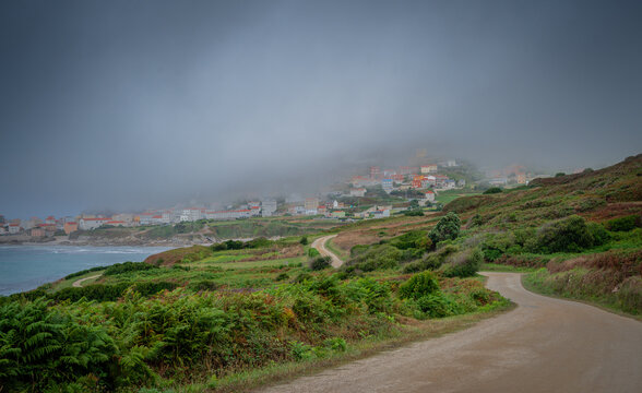 A dense, dark fog covers part of a coastal village