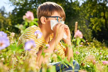 Child with hay fever sneezes in handkerchief on meadow