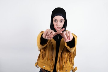young beautiful muslim woman wearing hijab and yellow jacket over white background has rejection...
