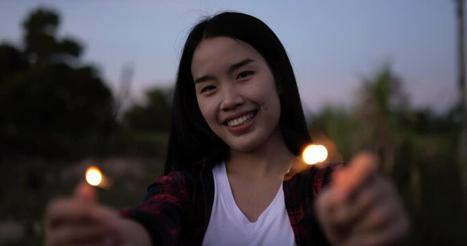 Asian beautiful woman holding fireworks burning sparkler playing in New year festival, Dressed in plaid shirt, waving hands, smiling and looking at the camera, she enjoy on new year's party night