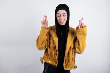 young beautiful muslim woman wearing hijab and yellow jacket over white background holding fingers...