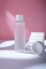 Transparent cosmetics toner bottle with concrete decorative elements on pink backdrop in harsh light mockup, no brand template