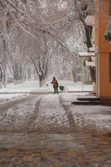 Janitor or sweeper in orange jacket cleaning city streets from snow with showel. snow removal in...