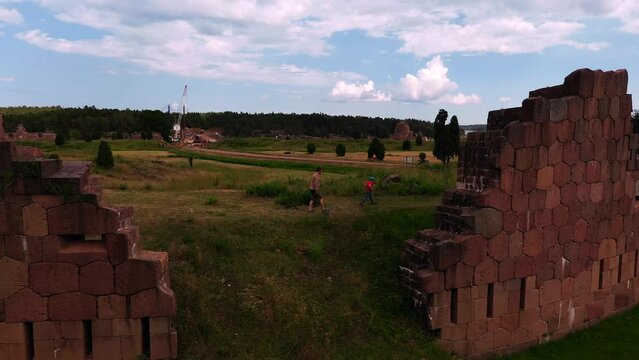 Aerial view of man and a boy walking in middle of Bomarsund castle ruins, in Aland, Finland - low, tracking, drone shot