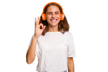 Young caucasian woman listening to music with headphones isolated cheerful and confident showing ok...