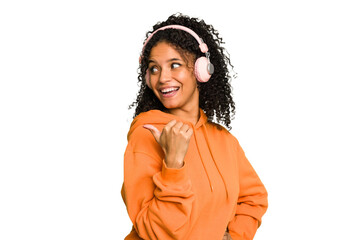 Young Brazilian woman listening to music with headphones isolated points with thumb finger away, laughing and carefree.