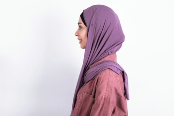 Profile portrait of nice young beautiful muslim woman wearing hijab and pink jacket over white background look empty space toothy smile
