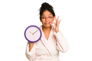 Young brazilian woman wearing a pajama holding a clock isolated with fingers on lips keeping a secret.