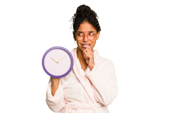 Young brazilian woman wearing a pajama holding a clock isolated relaxed thinking about something looking at a copy space.