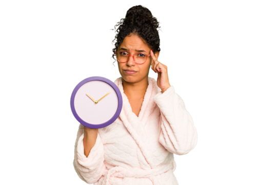 Young brazilian woman wearing a pajama holding a clock isolated pointing temple with finger, thinking, focused on a task.