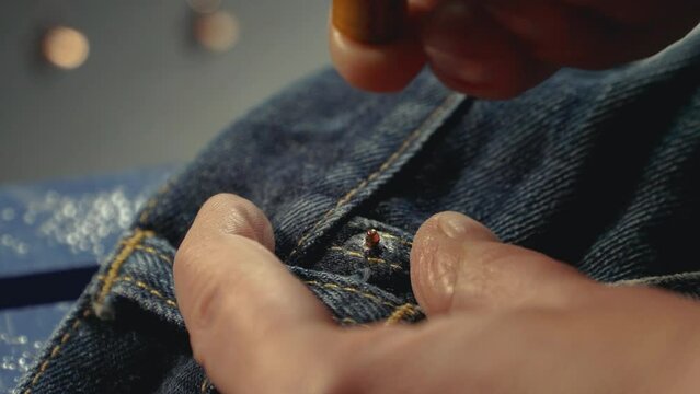 A tailor seamstress inserts metal rivets on jeans with a special machine in workshop repairing old denim clothes. Small family business, tailoring and repair of clothes, handmade. Close-up