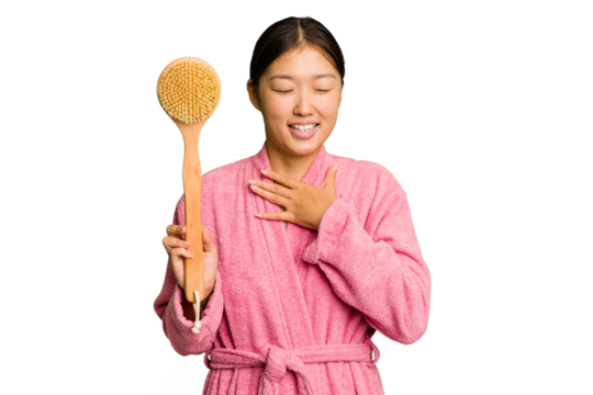 Young asian woman holding a shower brush isolated laughs out loudly keeping hand on chest.